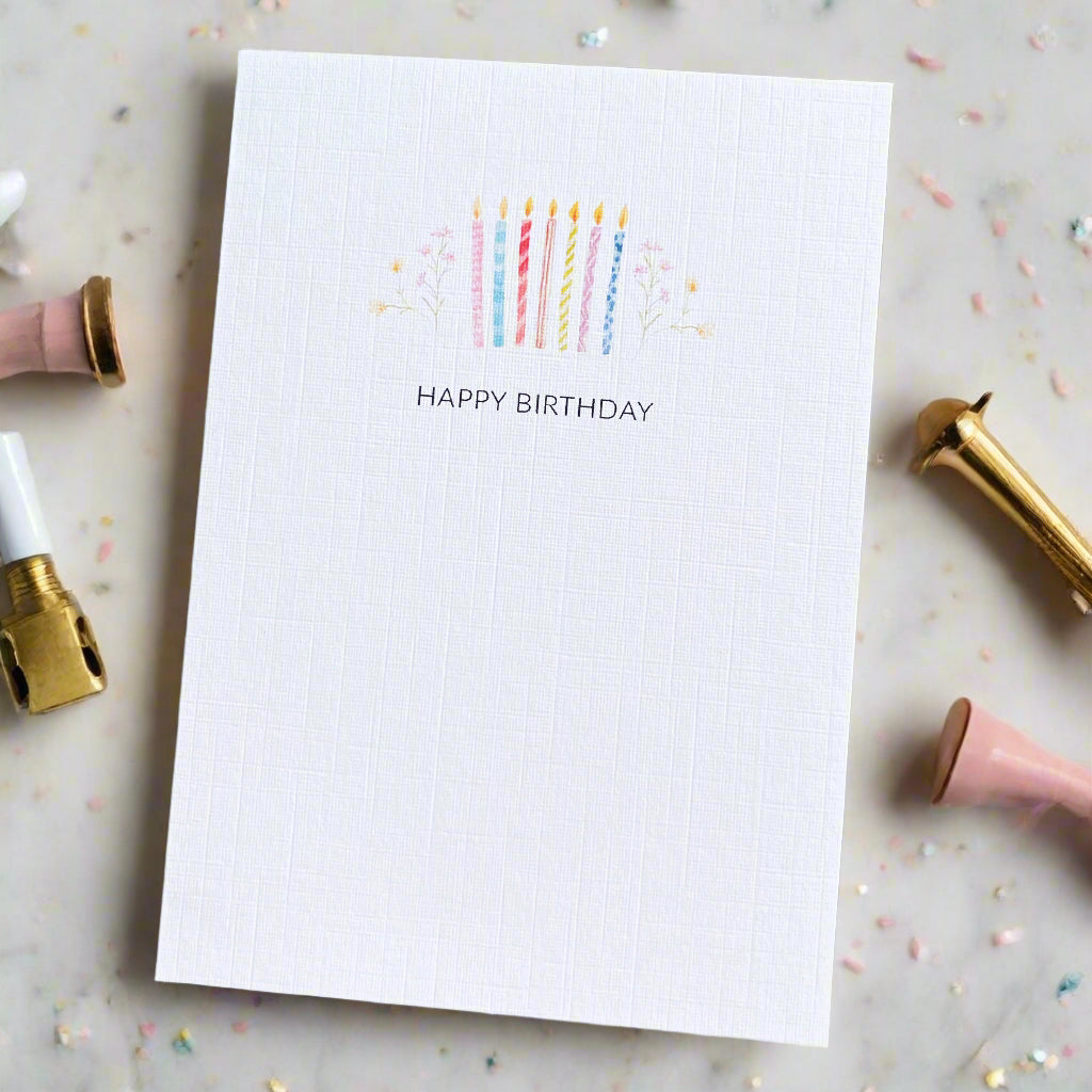 White card with colorful candles and 'Happy Birthday' text on a marble surface